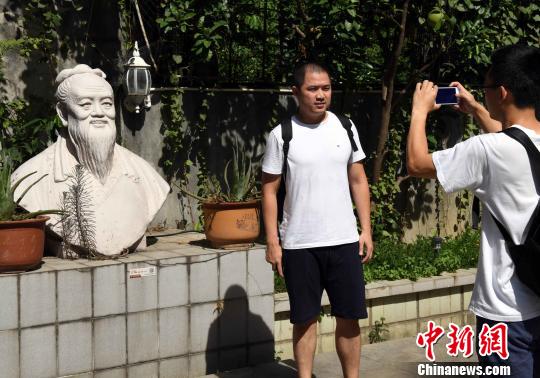 一名男青年在陈一帆雕塑艺术馆前与陈一帆创作的孔子塑像合影。　记者刘可耕 摄